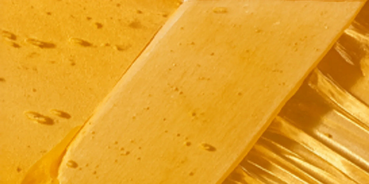 Close-up of translucent gold-coloured wax spread with a wooden spatula