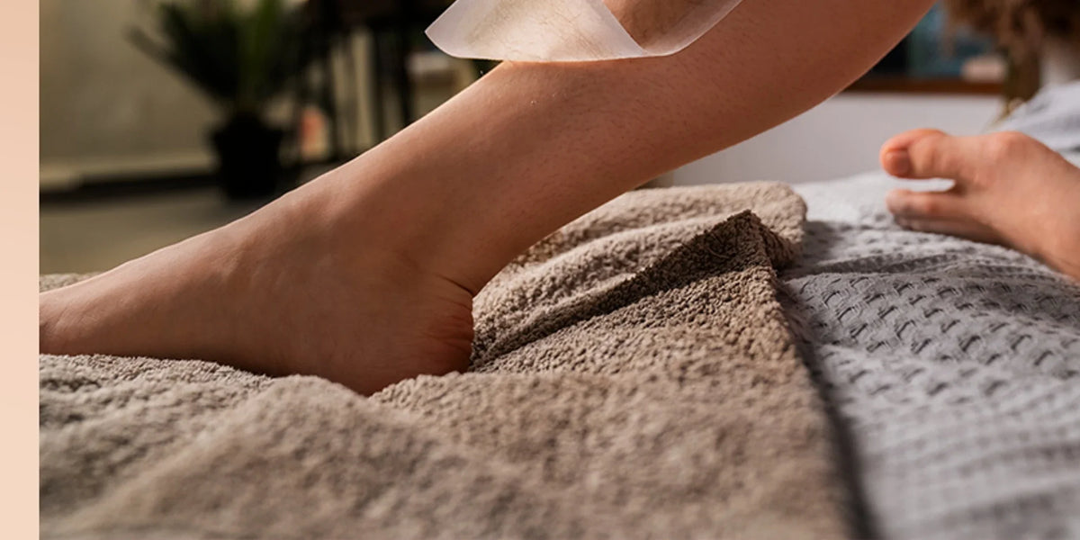 Waxing strip being lifted from a lower leg resting on folded towels