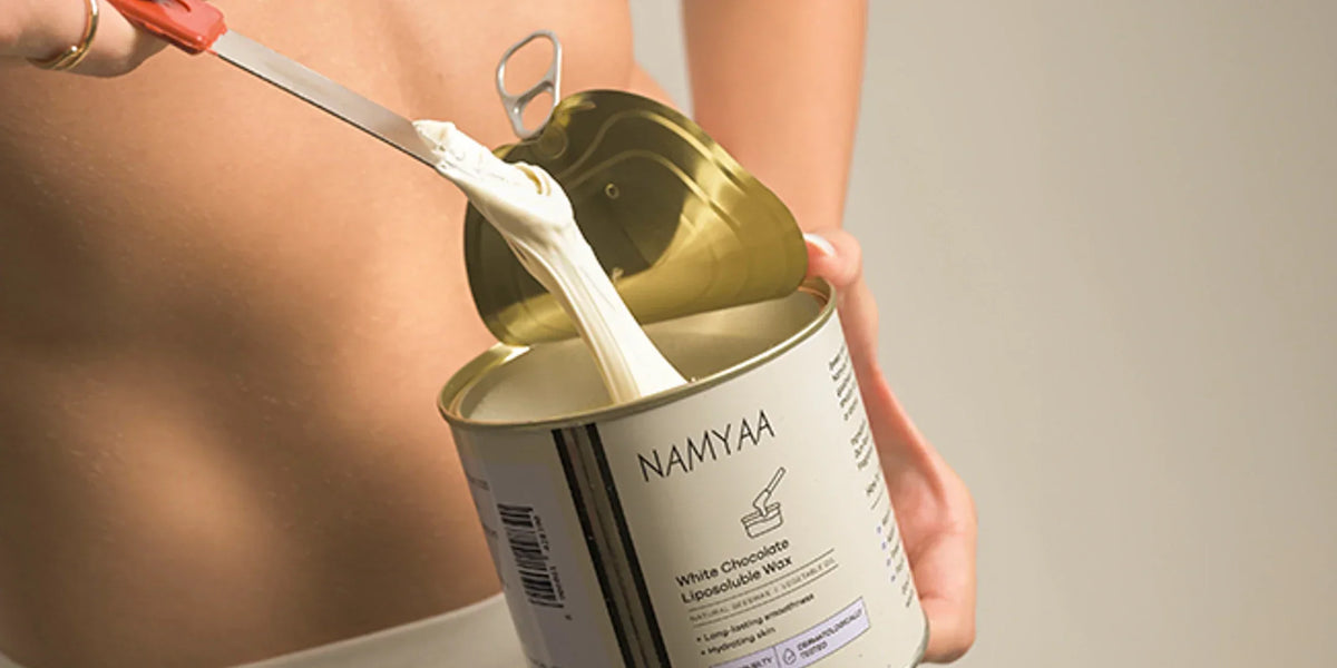 Open Namyaa White Chocolate Liposoluble Wax tin with creamy wax lifted on a spatula