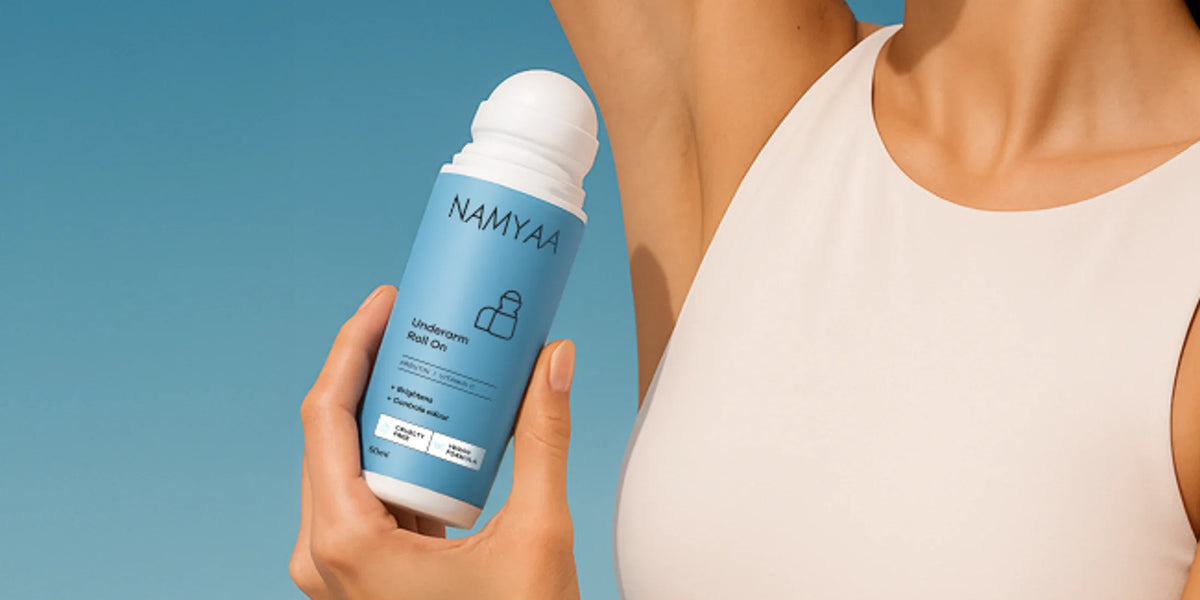Woman in a white sleeveless top holding Namyaa Underarm Roll-On against a blue background