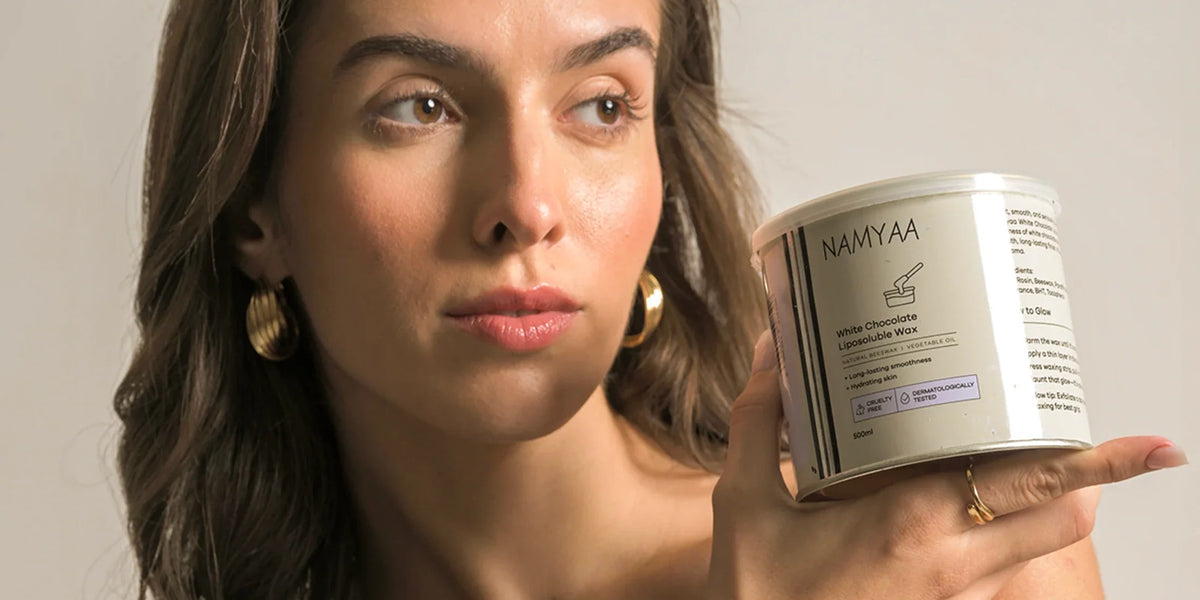 Woman holding a Namyaa White Chocolate Liposoluble Wax tin beside her face