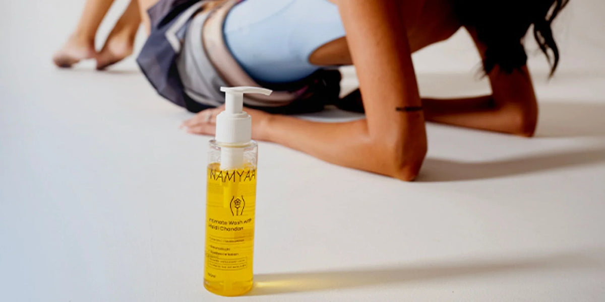 Namyaa intimate wash bottle in the foreground with a woman relaxing behind it