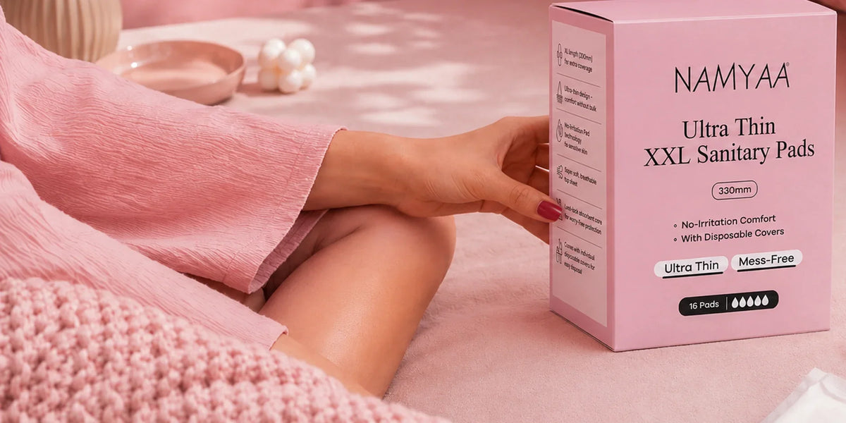 Woman in pink loungewear holding a Namyaa Ultra Thin XXL Sanitary Pads box on a bed