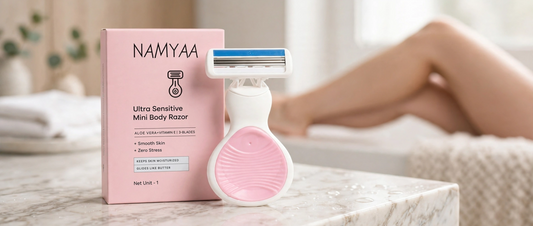 Namyaa Ultra Sensitive Mini Body Razor standing next to its pink box packaging on marble counter