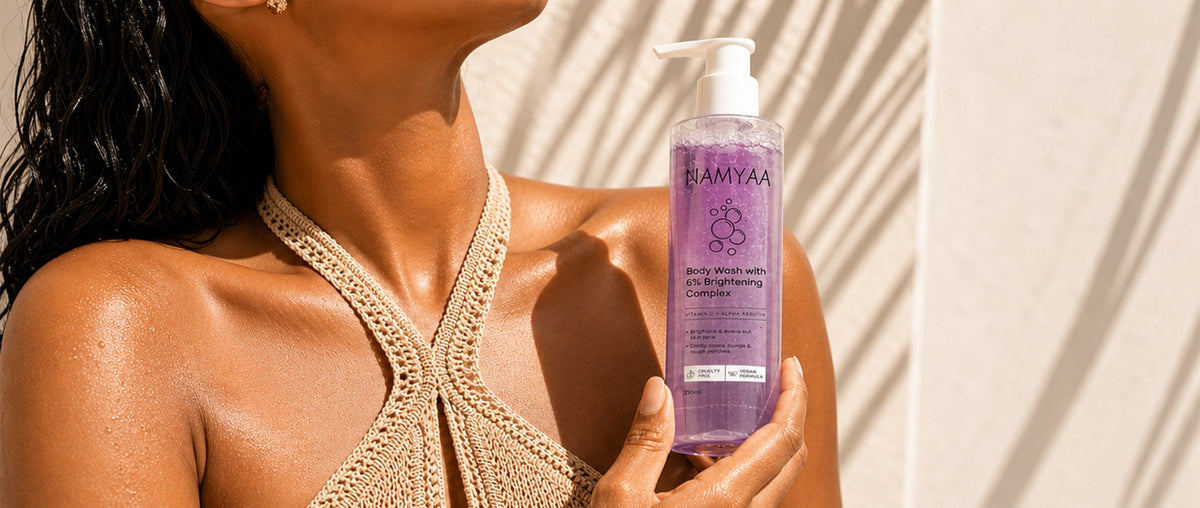 Close-up of Namyaa purple brightening body wash bottle featuring Vitamin C and Alpha Arbutin, held by a woman to showcase glowing, even-toned skin.