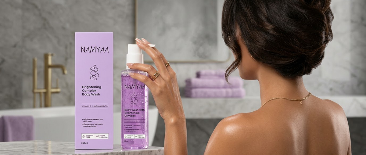 A woman seen from behind reaching toward a pump bottle and outer box of purple Namyaa Brightening Complex Body Wash in a modern bathroom setup.