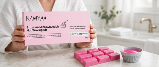 Woman in bathrobe holding 200gm pink Namyaa Brazilian Microwaveable Hot Waxing Kit box next to solid wax cubes and melted wax