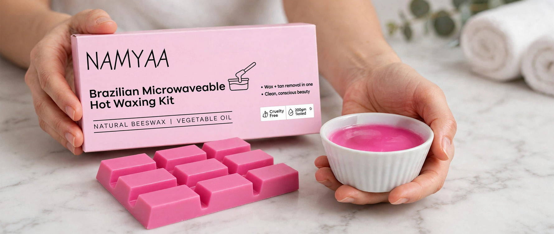 Hands holding Namyaa microwaveable hot wax kit box with pink stripless wax cubes and melted wax for hair removal