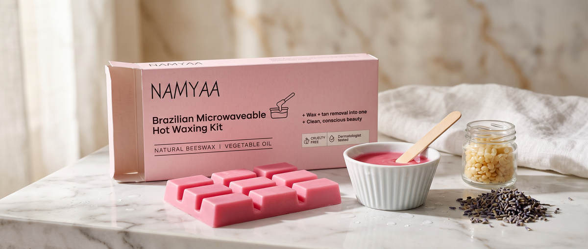 A pink solid wax block shaped like a chocolate bar next to a bowl of melted pink wax, a jar of wax beads, and the Namyaa Brazilian Microwaveable Hot Waxing Kit box.