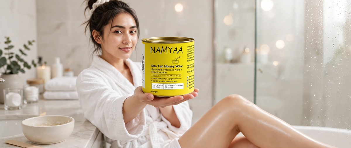 Namyaa De-Tan Honey Wax tin enriched with Kojic Acid and Niacinamide held by a woman sitting next to a bathtub.