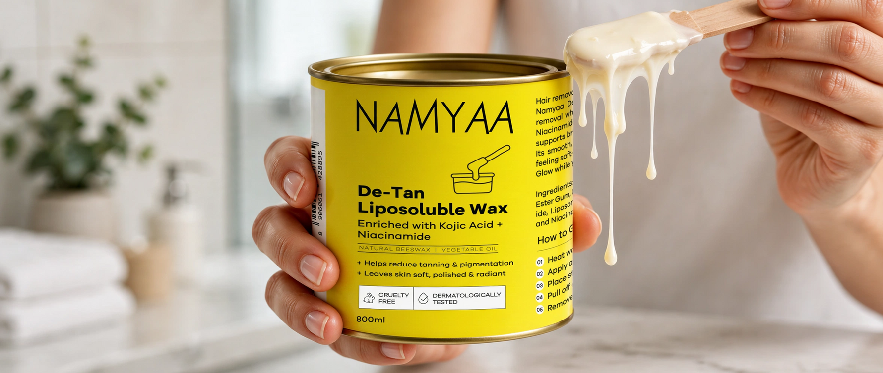 Namyaa De-Tan Liposoluble Wax with Kojic Acid and Niacinamide in a yellow tin with melted wax on a spatula.