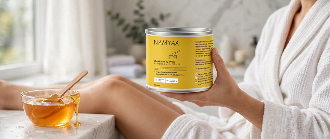 Namyaa Gold Honey Wax tin held in hand next to a glass bowl of honey wax with wooden spatula