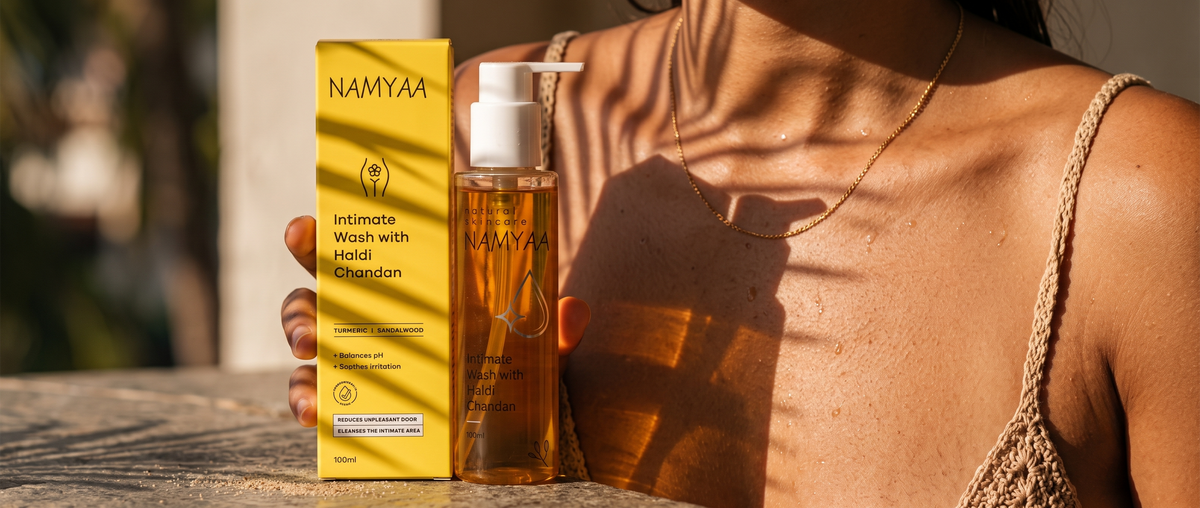 A person holding the yellow packaging box and pump bottle of Namyaa Intimate Wash with Haldi Chandan under warm, dappled sunlight.