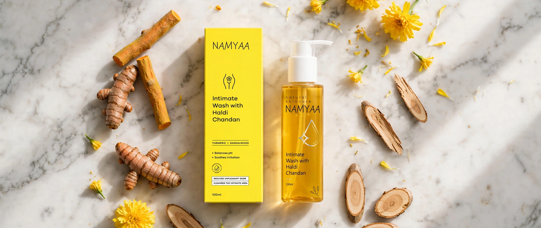 Flat lay of Namyaa Intimate Wash with Haldi Chandan bottle and box surrounded by fresh turmeric, sandalwood, and yellow flowers