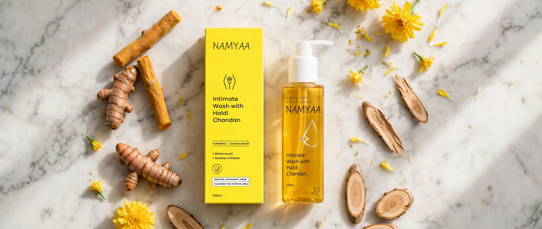 Flat lay of Namyaa Intimate Wash with Haldi Chandan bottle and box surrounded by fresh turmeric, sandalwood, and yellow flowers
