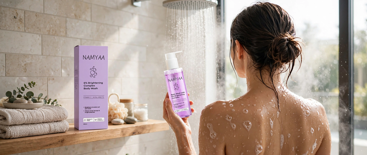 Namyaa 6% Brightening Complex Body Wash with Vitamin C and Alpha Arbutin held by a woman in the shower next to its purple product box.
