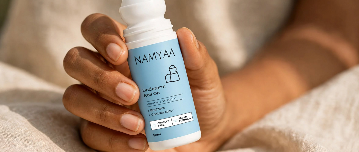 Close-up of a hand holding a bottle of Namyaa Underarm Roll On deodorant against a neutral linen background.