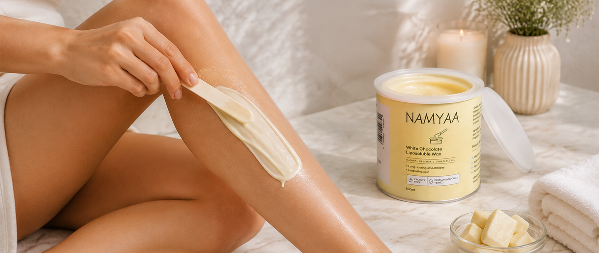 A woman applying Namyaa White Chocolate Liposoluble Wax on her lower leg using a wooden spatula with the product tub nearby.