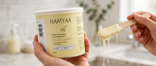 Hand holding Namyaa White Chocolate Liposoluble Wax tin while scooping dripping wax with a wooden spatula